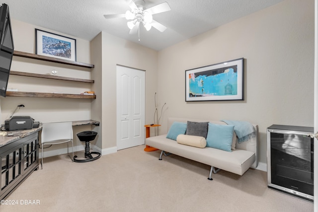 sitting room with ceiling fan, a textured ceiling, light carpet, and wine cooler