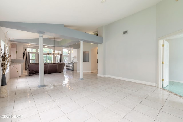 empty room featuring light tile patterned floors, an inviting chandelier, vaulted ceiling, and decorative columns