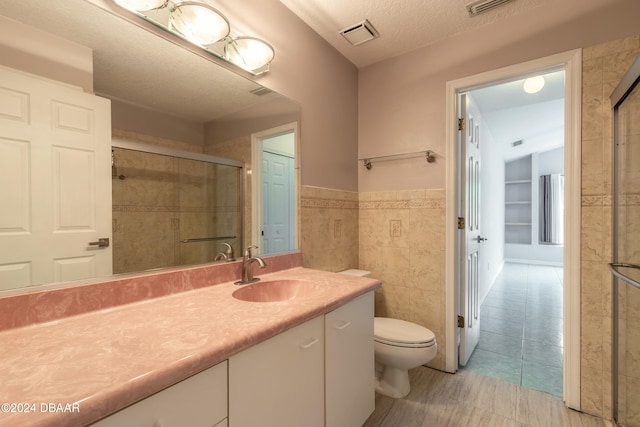 bathroom featuring tile patterned flooring, a textured ceiling, vanity, toilet, and tile walls