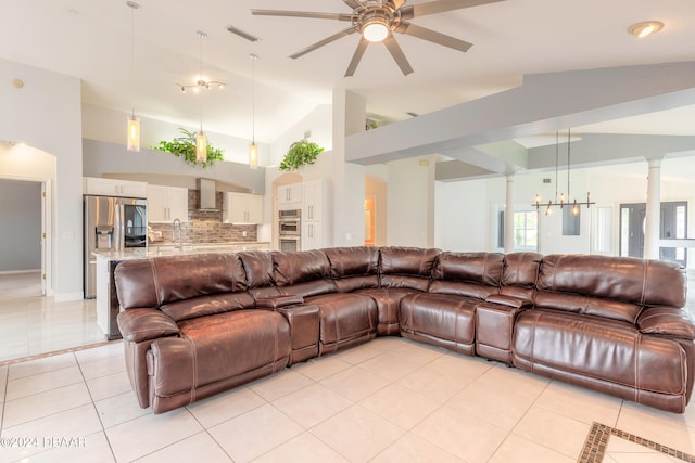 living room featuring ceiling fan with notable chandelier, light tile patterned floors, ornate columns, and high vaulted ceiling