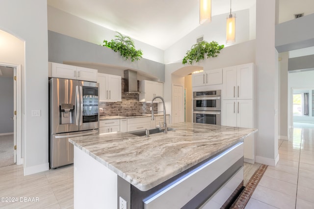 kitchen featuring stainless steel appliances, high vaulted ceiling, hanging light fixtures, white cabinets, and wall chimney range hood