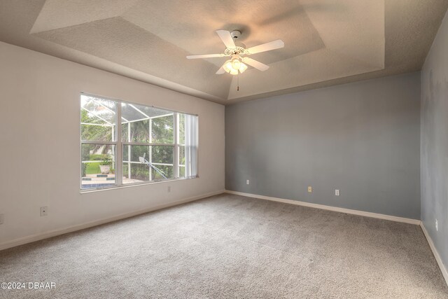 carpeted spare room with a textured ceiling, ceiling fan, and a tray ceiling