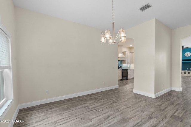 unfurnished room with an inviting chandelier and light hardwood / wood-style flooring