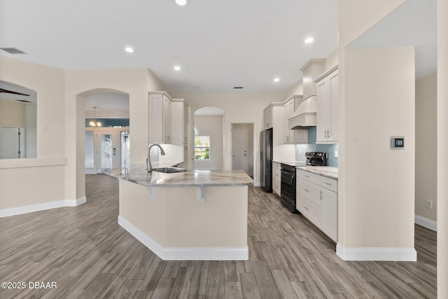 kitchen with white cabinetry, light stone countertops, light wood-type flooring, and black appliances