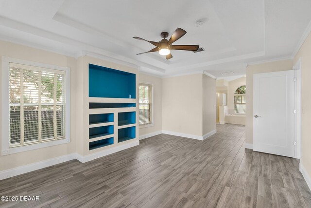 unfurnished living room with wood-type flooring, ornamental molding, ceiling fan, and a tray ceiling