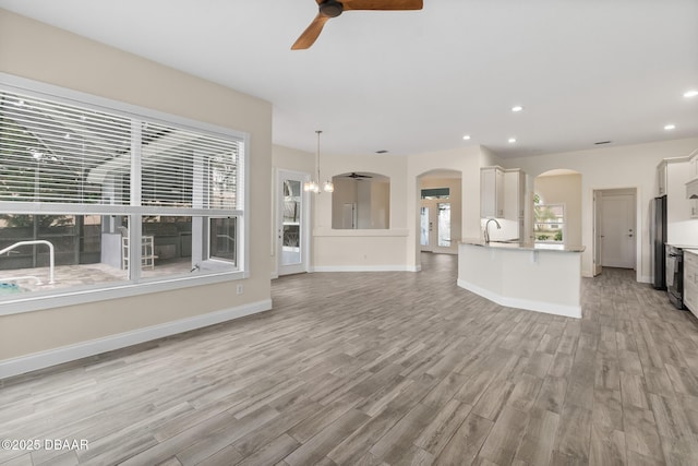 unfurnished living room with ceiling fan with notable chandelier and light hardwood / wood-style floors