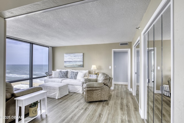 living area featuring light wood finished floors, a textured ceiling, visible vents, and a wall of windows