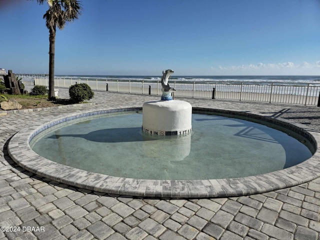 view of pool with a patio area, a water view, and a view of the beach