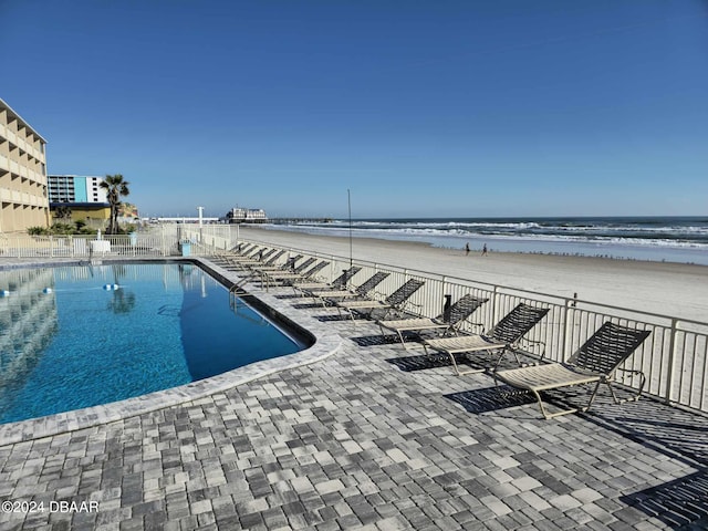 view of pool featuring a patio area, a water view, and a view of the beach