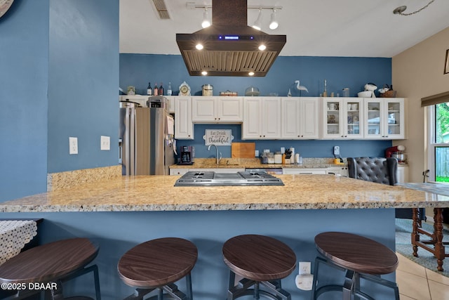 kitchen with island exhaust hood, stainless steel appliances, visible vents, glass insert cabinets, and a peninsula