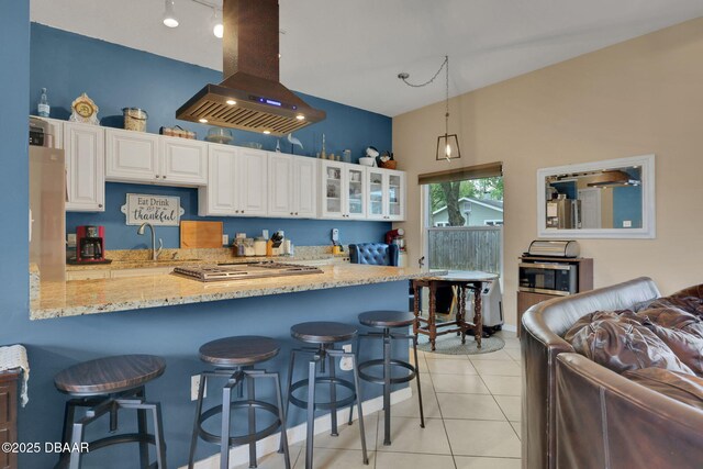 kitchen featuring glass insert cabinets, a breakfast bar, light stone counters, island exhaust hood, and light tile patterned flooring