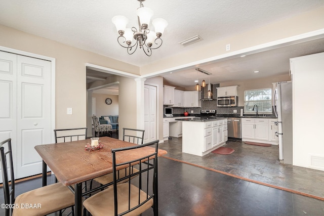 dining area featuring a textured ceiling, decorative columns, sink, an inviting chandelier, and dark wood-type flooring