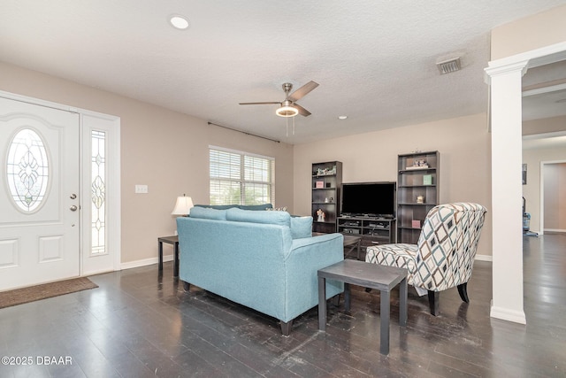 living room featuring decorative columns, ceiling fan, dark wood-type flooring, and a textured ceiling