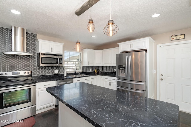 kitchen with appliances with stainless steel finishes, white cabinets, wall chimney range hood, sink, and hanging light fixtures