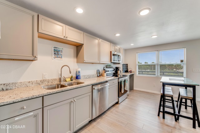 kitchen with light wood-type flooring, appliances with stainless steel finishes, sink, and light stone countertops