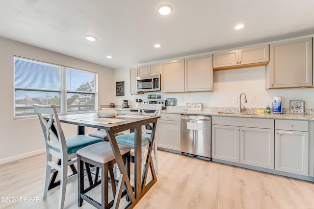 kitchen with light wood-type flooring, sink, light stone counters, and appliances with stainless steel finishes