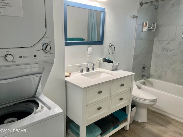 full bathroom featuring wood-type flooring, toilet, stacked washing maching and dryer, tiled shower / bath, and vanity