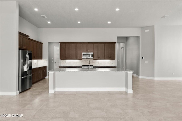 kitchen with light stone counters, an island with sink, appliances with stainless steel finishes, and a sink