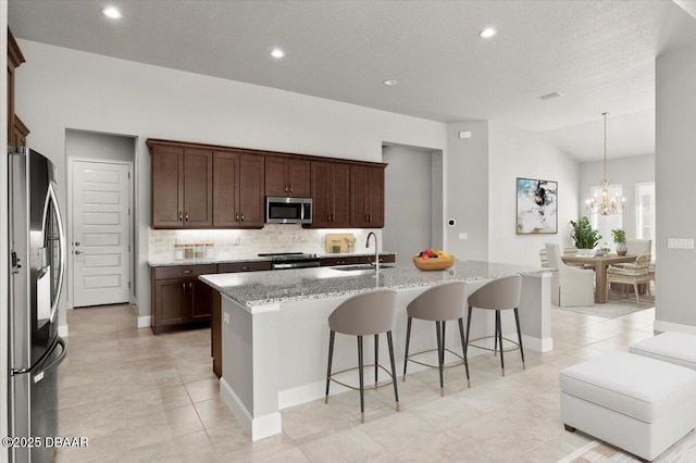 kitchen with a breakfast bar area, light stone counters, a sink, stainless steel appliances, and a notable chandelier