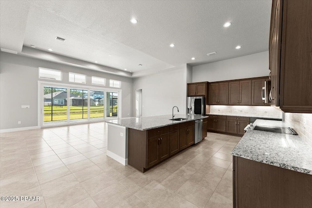 kitchen with a kitchen island with sink, a sink, decorative backsplash, appliances with stainless steel finishes, and open floor plan