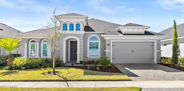 view of front of house with a front yard, roof with shingles, stucco siding, decorative driveway, and an attached garage