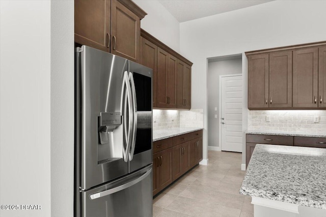 kitchen featuring light tile patterned floors, light stone counters, baseboards, stainless steel fridge with ice dispenser, and backsplash