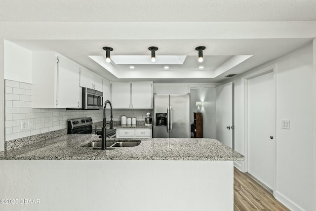 kitchen featuring stainless steel appliances, kitchen peninsula, sink, and stone counters