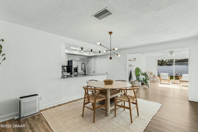 dining area featuring ceiling fan with notable chandelier, heating unit, a textured ceiling, and light hardwood / wood-style flooring