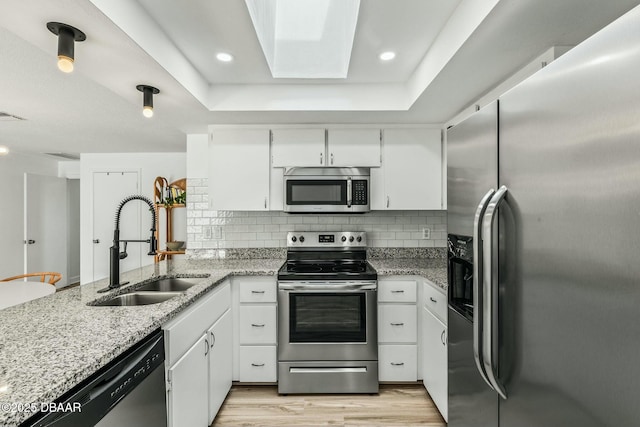 kitchen with sink, appliances with stainless steel finishes, light stone countertops, decorative backsplash, and white cabinets