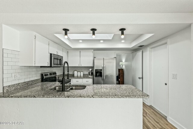 kitchen featuring stainless steel appliances, backsplash, a raised ceiling, a sink, and a peninsula