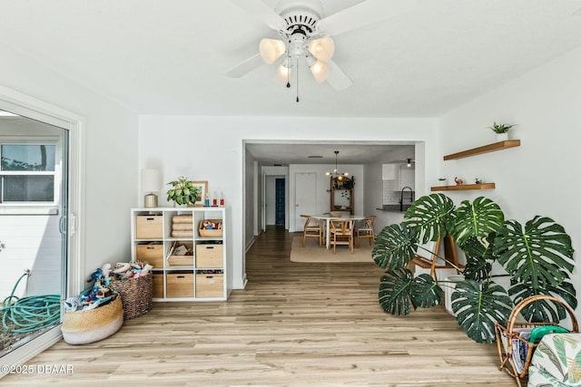 sitting room with ceiling fan with notable chandelier and light hardwood / wood-style floors