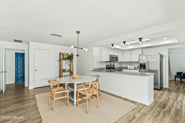 kitchen featuring appliances with stainless steel finishes, stone countertops, pendant lighting, white cabinetry, and kitchen peninsula