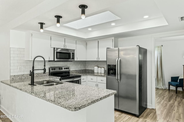 kitchen with stainless steel appliances, a tray ceiling, kitchen peninsula, and white cabinets