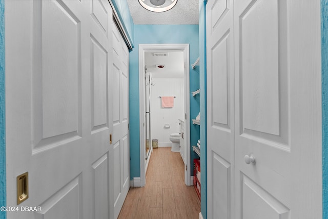 hallway with light wood-type flooring and a textured ceiling