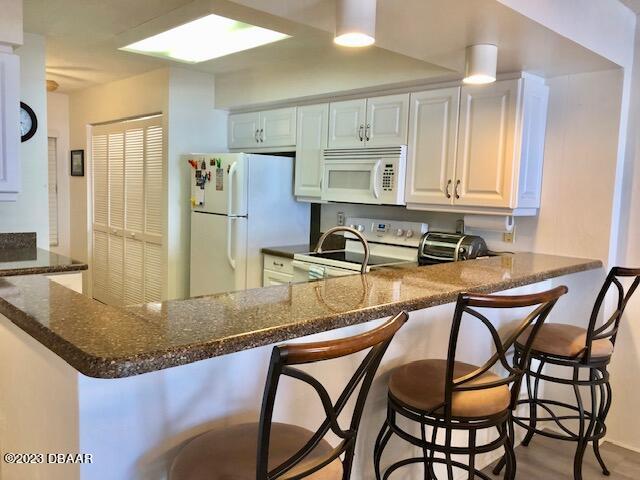 kitchen with white cabinets, kitchen peninsula, white appliances, and a breakfast bar