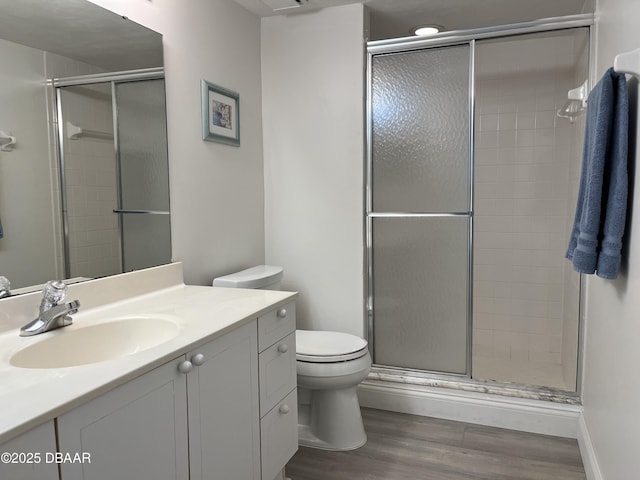 bathroom with toilet, wood finished floors, vanity, and a shower stall