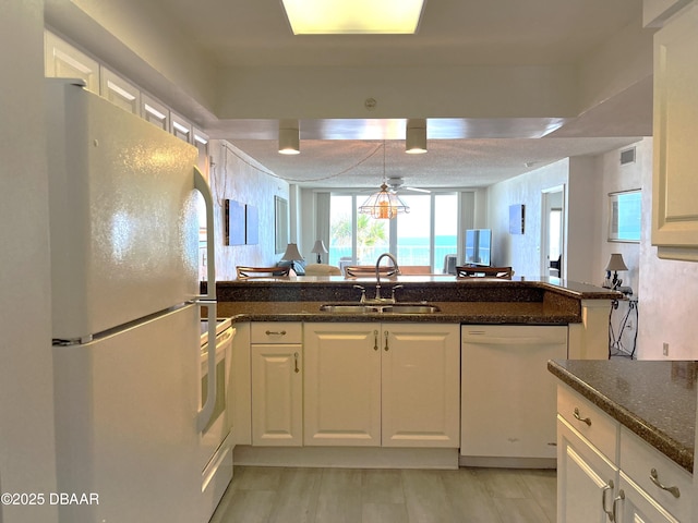 kitchen with white appliances, dark stone countertops, white cabinetry, and a sink