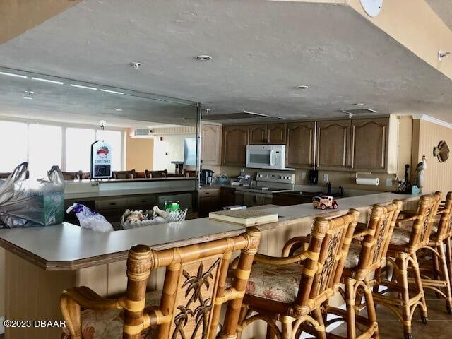 kitchen featuring stainless steel electric stove, a kitchen bar, a textured ceiling, and kitchen peninsula