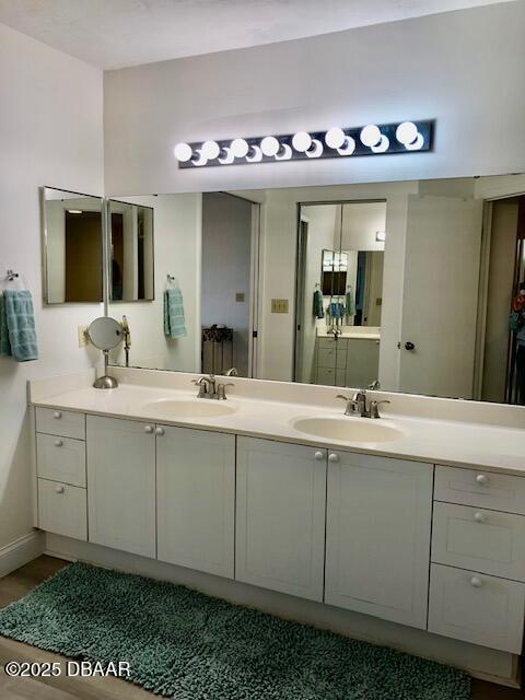 full bathroom with double vanity, baseboards, a sink, and wood finished floors