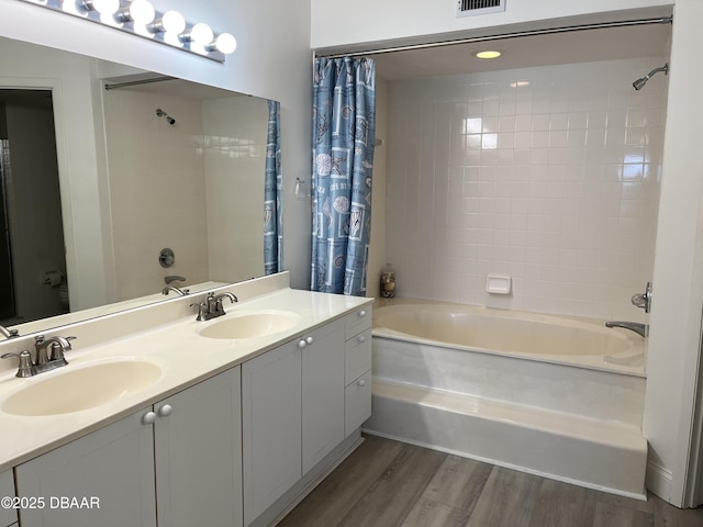 full bath featuring shower / bath combo, double vanity, a sink, and wood finished floors