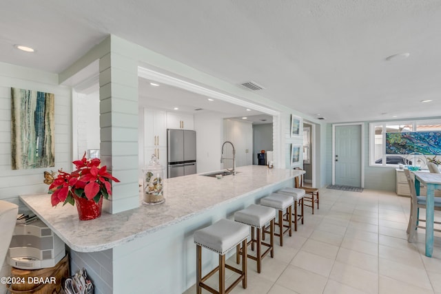 kitchen with light stone countertops, sink, light tile patterned floors, stainless steel fridge, and white cabinets