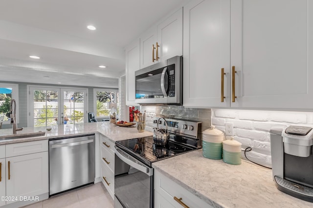 kitchen with sink, stainless steel appliances, light stone counters, backsplash, and white cabinets