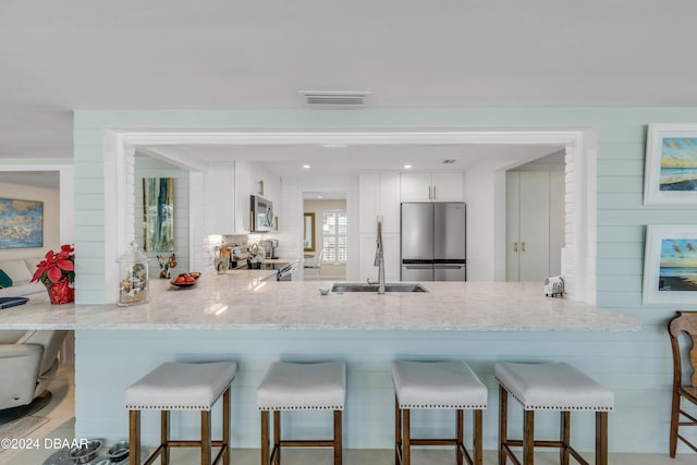 kitchen with white cabinetry, sink, stainless steel appliances, a kitchen breakfast bar, and kitchen peninsula