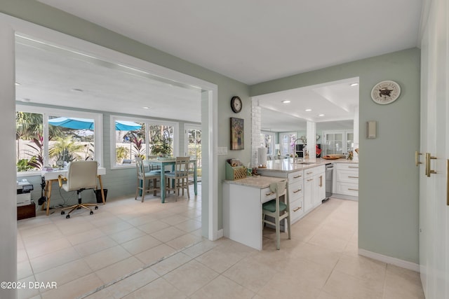 kitchen featuring sink, kitchen peninsula, light tile patterned floors, light stone counters, and white cabinetry