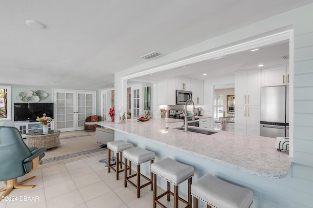 kitchen with kitchen peninsula, appliances with stainless steel finishes, french doors, a breakfast bar, and white cabinets