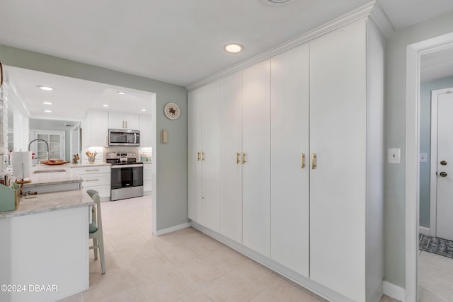 kitchen with appliances with stainless steel finishes, backsplash, light stone counters, a breakfast bar, and white cabinets