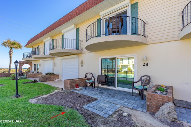 back of property featuring a balcony, a garage, a patio area, and a lawn