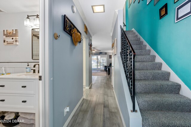 staircase featuring ceiling fan, sink, ornamental molding, and hardwood / wood-style flooring