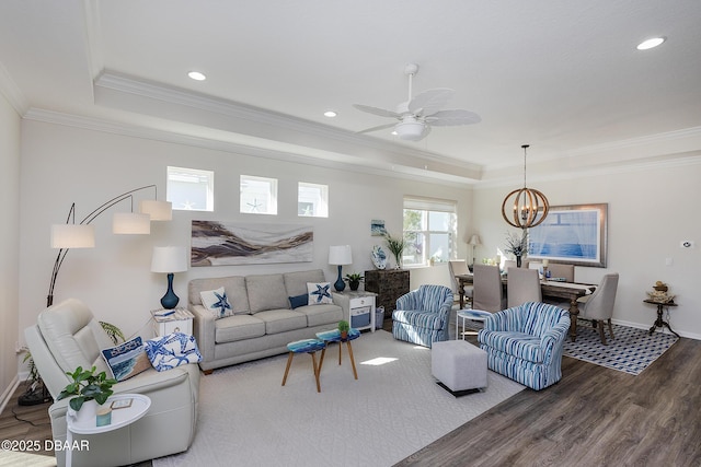 living room featuring ceiling fan with notable chandelier, wood-type flooring, ornamental molding, and a raised ceiling