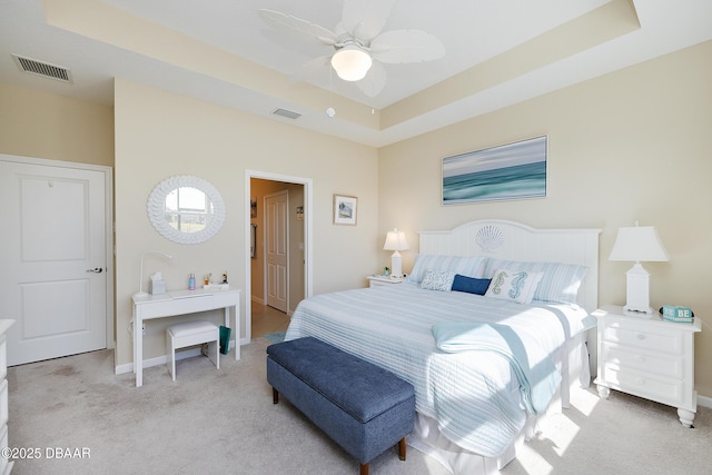 bedroom with ceiling fan, light colored carpet, and a tray ceiling